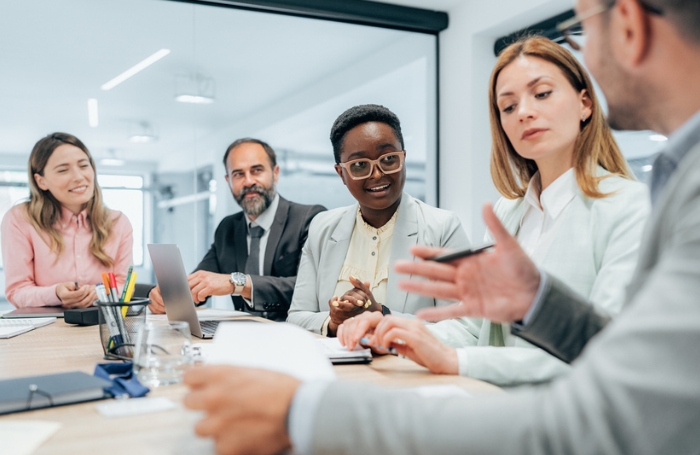 A group of people sitting around a desk in discussion GC LARGEjpg People discussing work in an office meeting
