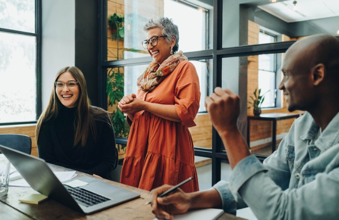 A team of mixed race professional looking relaxed and smiling aorund a table in an office LARGEjpg