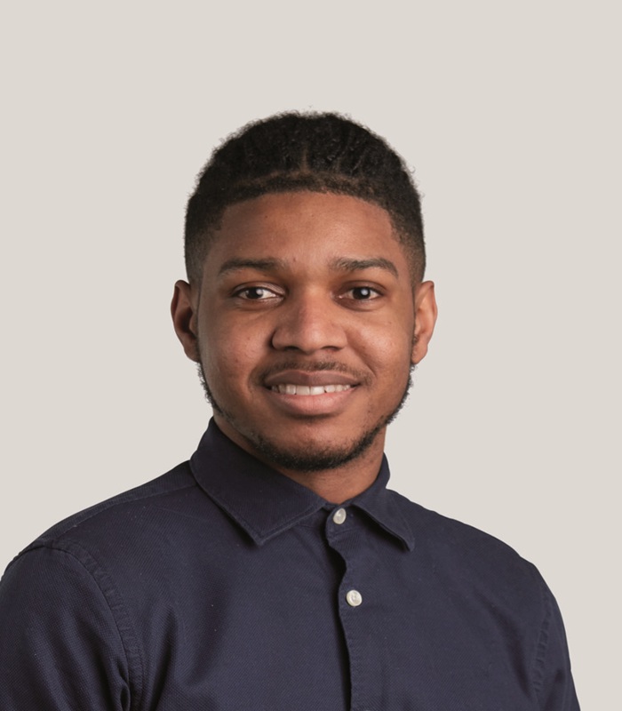 DGM Headshot700x800jpg Portrait of Dorréll Gayle-Menzie, a young man smiling facing the camera in a smart black button up shirt.