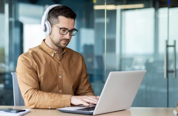 Man sitting a desk wearing headphones and studying at a laptop GC LARGEjpg