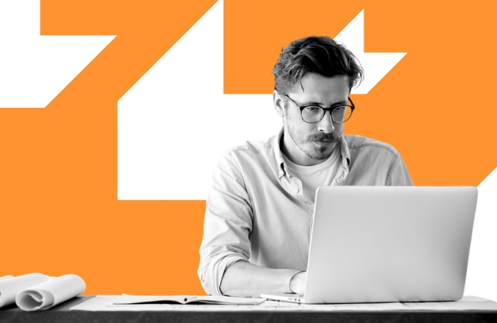 Man wearing glasses sitting behind a laptop on an orange background GC LARGEjpg Man wearing glasses sitting behind a laptop on an orange background