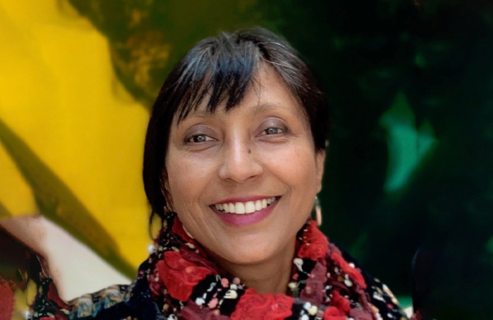 Sumita Singha wearing a scarf and smiling in front of abstract background 700jpg