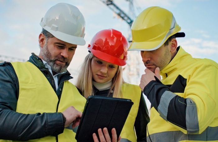 Three architects on a building site wearing highviz jackets and looking at a digital tablet GC LARGE Three architects on a building site wearing high visibility jackets and looking at a digital tablet