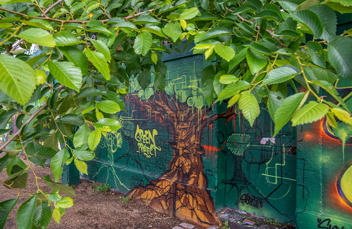 Tree leaves framing a painted wall mural of a tree trunk 700jpg