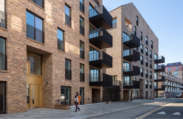 Woman walking past a group of modern enw buld social ousing apartments GC LARGEjpg