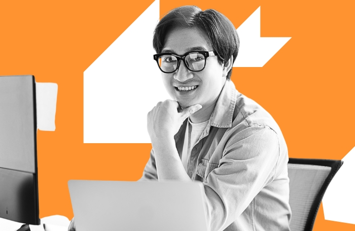 Young man sitting at a desk working on a computer smiling to the camera LARGEjpg
