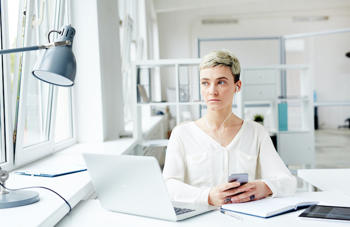 A woman sitting at at a desk wearing headphones while looking out of the windowjpg
