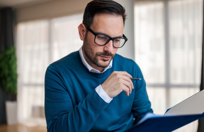 An architects in a blue sweater reading some papers at his desk GC LARGEjpg