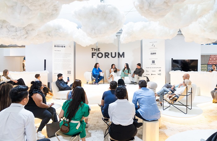 Gulf chapter Downtown Design700x455jpg Selection of people gathered around a stage set up for four particpants. There are faux clouds covering the ceiling and the word FORUM in large black letters hangs over the stage.
