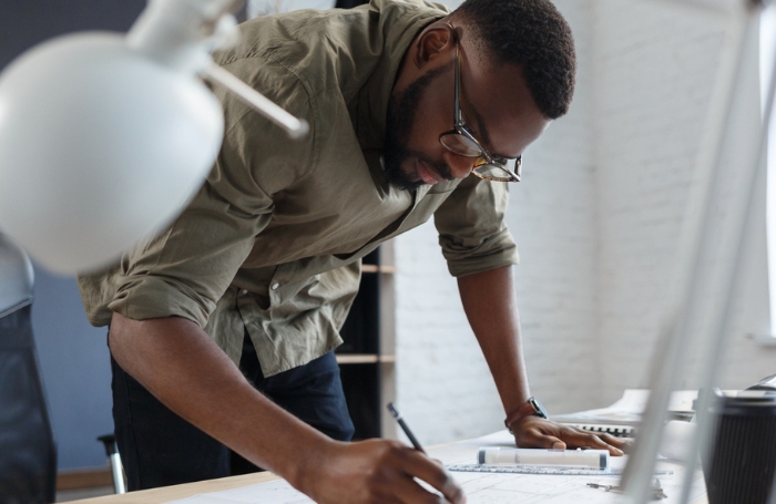 Male architect leaning over a diagram on a desk and making adjustments with a penciljpg Male architect leaning over a diagram on a desk and making adjustments with a pencil