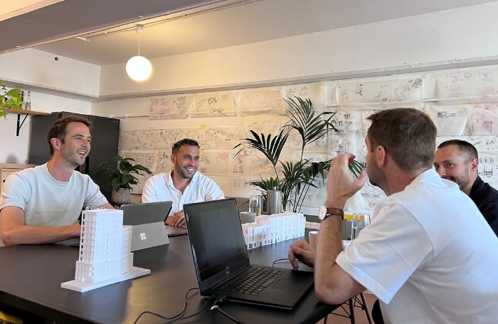 Two architects sitting at a desk smiling and discussing a project with clientsjpg Architects discussing work with clients in an office desk space