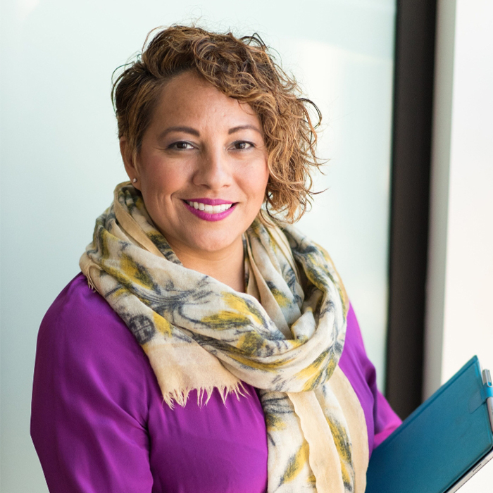 Woman with styled hair and scard smiling while holding an Ipadjpg