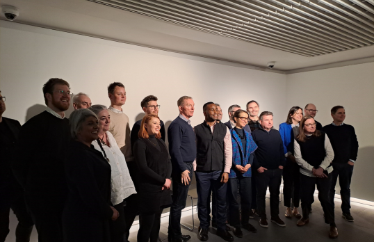 People lined up for formal photo as a group against a white wall background