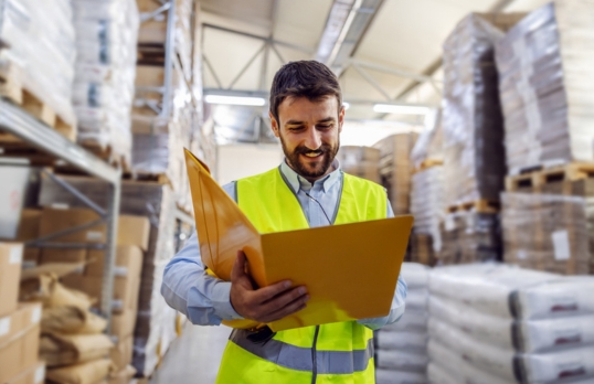 Peron in hi-vis yellow vest and carrying s clipboard in a construction material warehouse