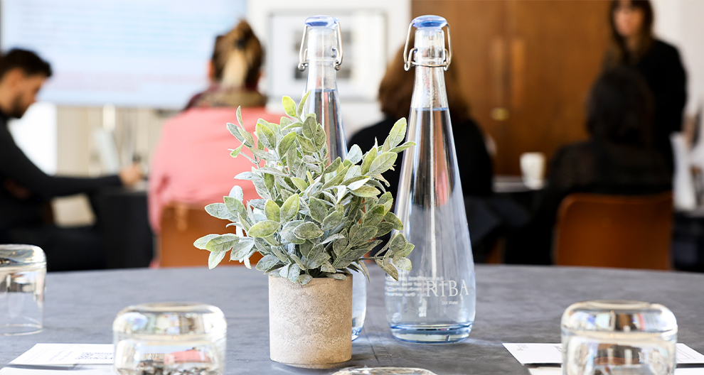 Meeting room set up of water bottle and glasses with people having a meeting in the background